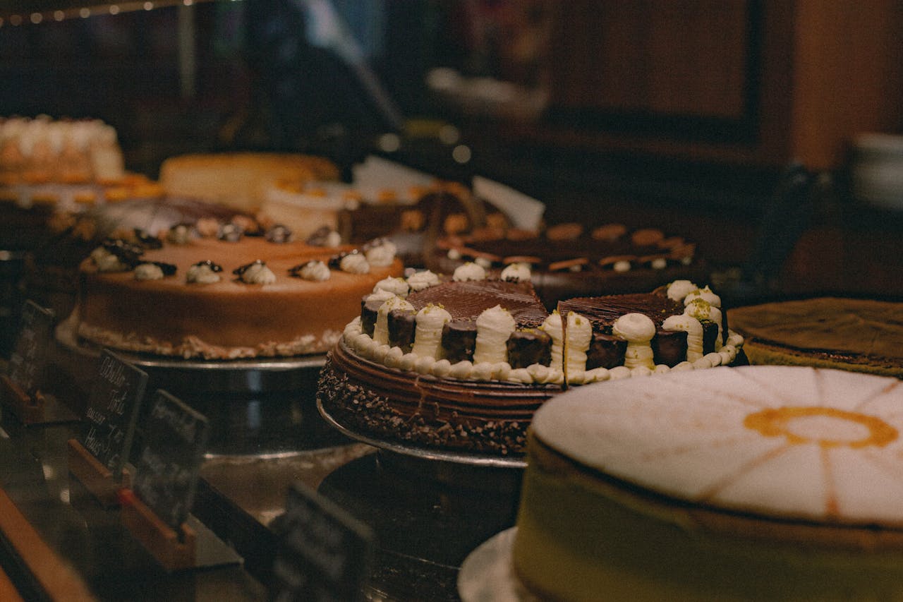 Close-up shot of various cakes in a bakery display case, showcasing different flavors and designs.