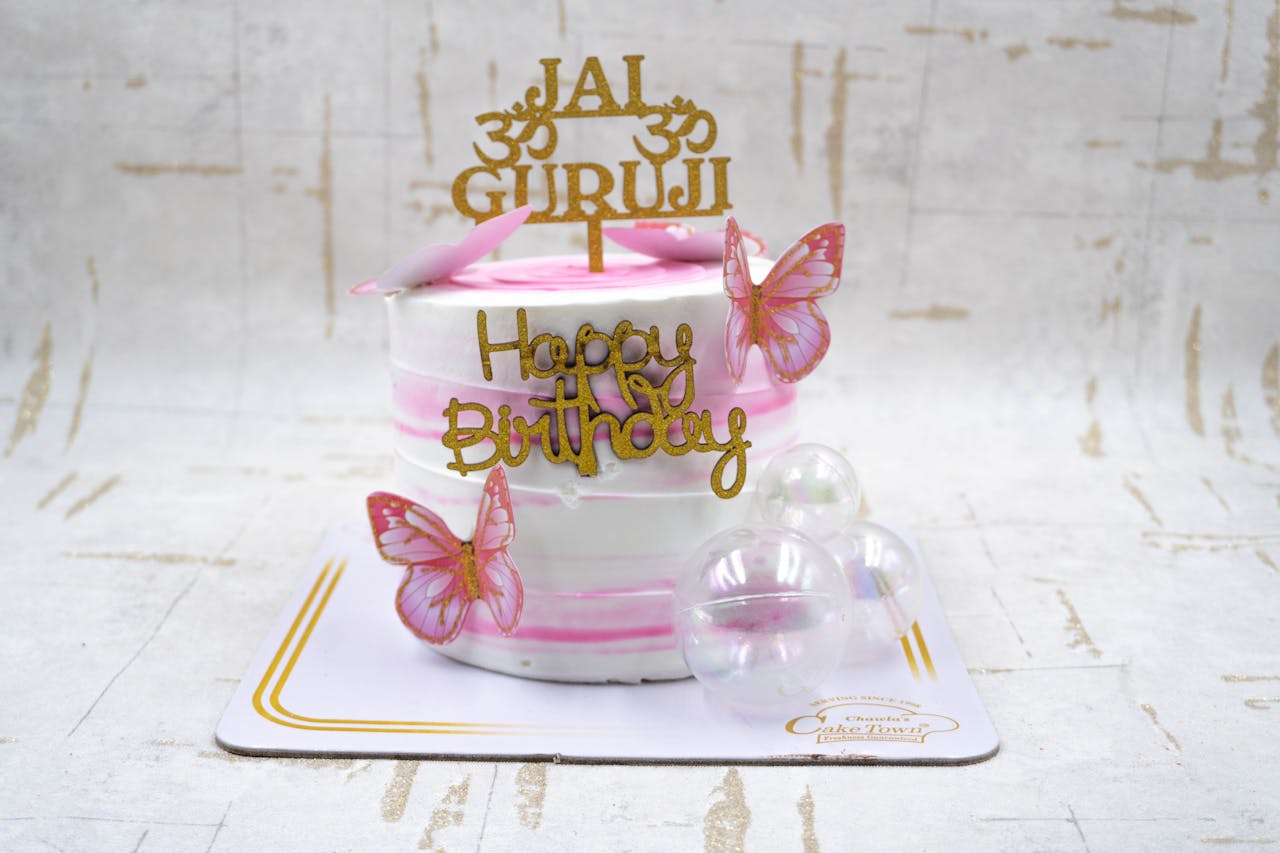 Home Stylish pink and white birthday cake with butterfly decorations and a Happy Birthday topper.